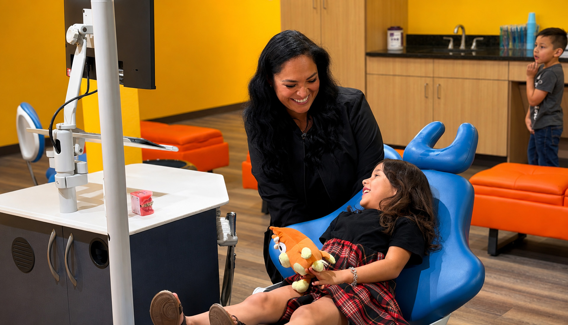 Staff Member Smiling With Young Girl Holding Stuffed Toy In Dental Chair